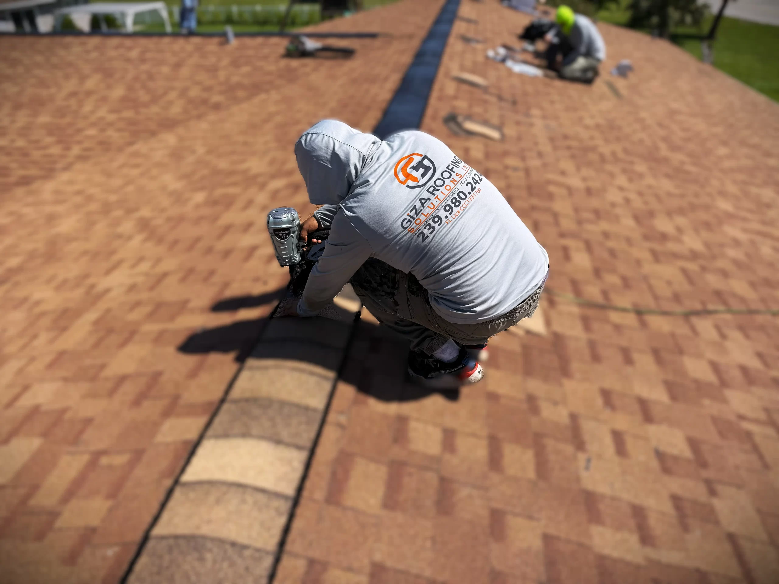 Overhead view of a Giza Roofing Solutions roofer installing shingles, with another worker in the background, demonstrating roof repair or installation.